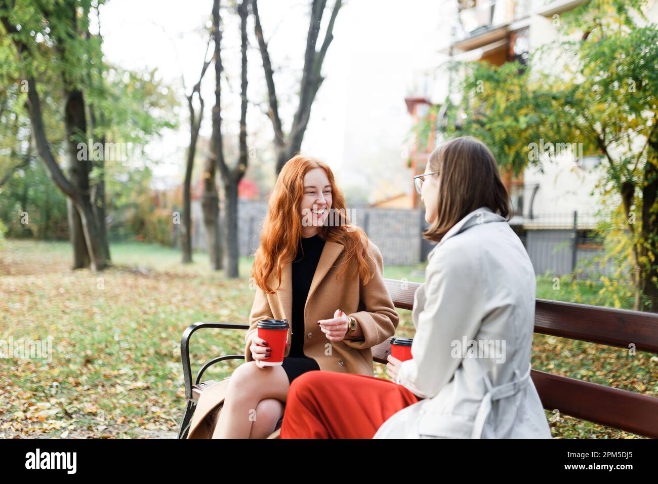 les filles s'amusent à s'asseoir avec des boissons chaudes dans le parc d'automne sur un banc Banque D'Images