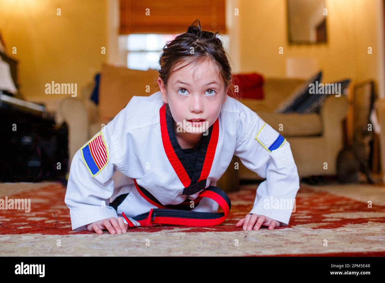 Une fille féroce en uniforme de Taekwondo fait des poussettes dans la salle de séjour Banque D'Images