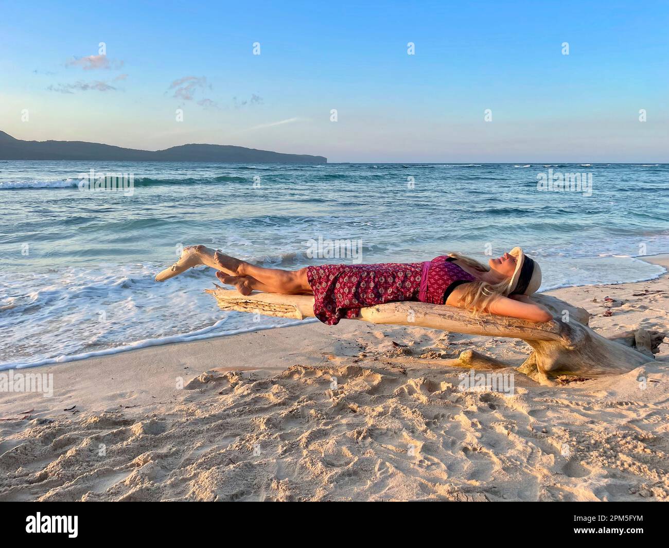 Femme dans la sundress couché sur le bois flotté sur la belle plage de sable blanc Banque D'Images