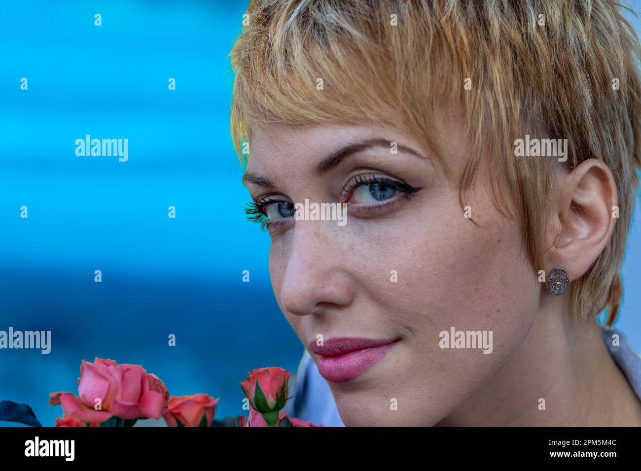 Portrait coloré d'une jeune femme aux cheveux blonds courts dehors dans la nature, odorant et appréciant de petites fleurs roses. Un cadeau de sa mère Banque D'Images