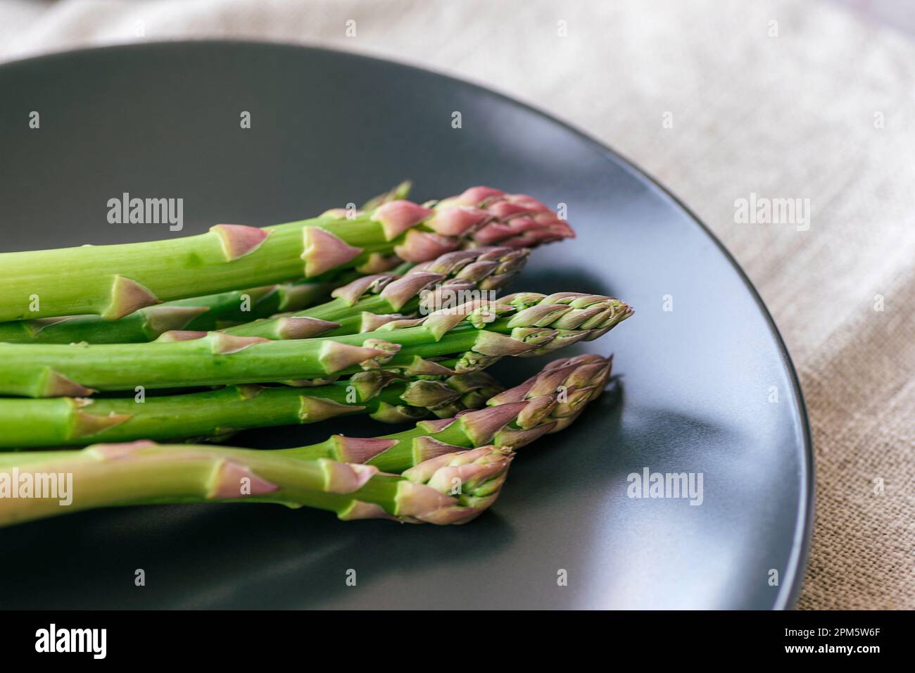 Asperges vertes fraîches sur une assiette noire sur une serviette grise. Concept alimentaire végétalien sain. Gros plan. Banque D'Images