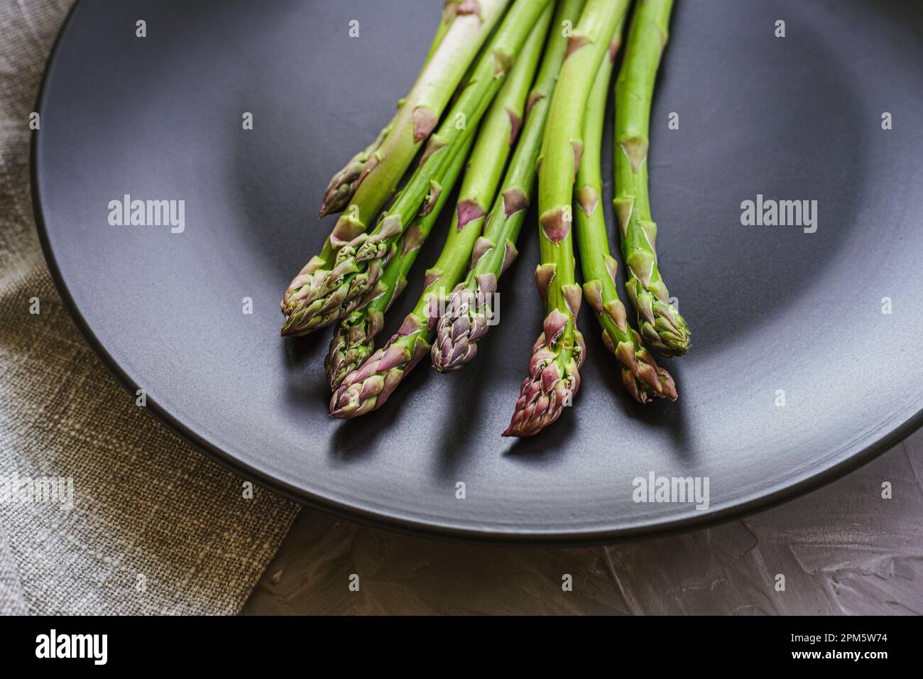 Asperges vertes fraîches sur plaque noire sur table en béton gris. Concept alimentaire végétalien sain. Gros plan. Banque D'Images