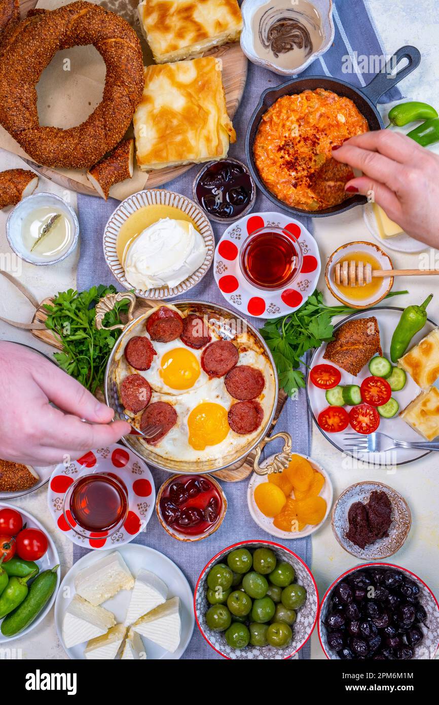 Table de petit-déjeuner traditionnelle turque avec œufs, sujuk. menemen, olives, kaymak, miel, simit, borek, légumes. Homme et femme qui prennent de la nourriture v Banque D'Images