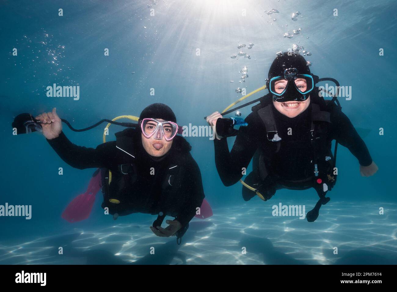 Gros plan de deux plongeurs heureux tenant leurs régulateurs dans leurs mains sous l'eau avec une langue dehors et souriant à la caméra avec le soleil vif Banque D'Images