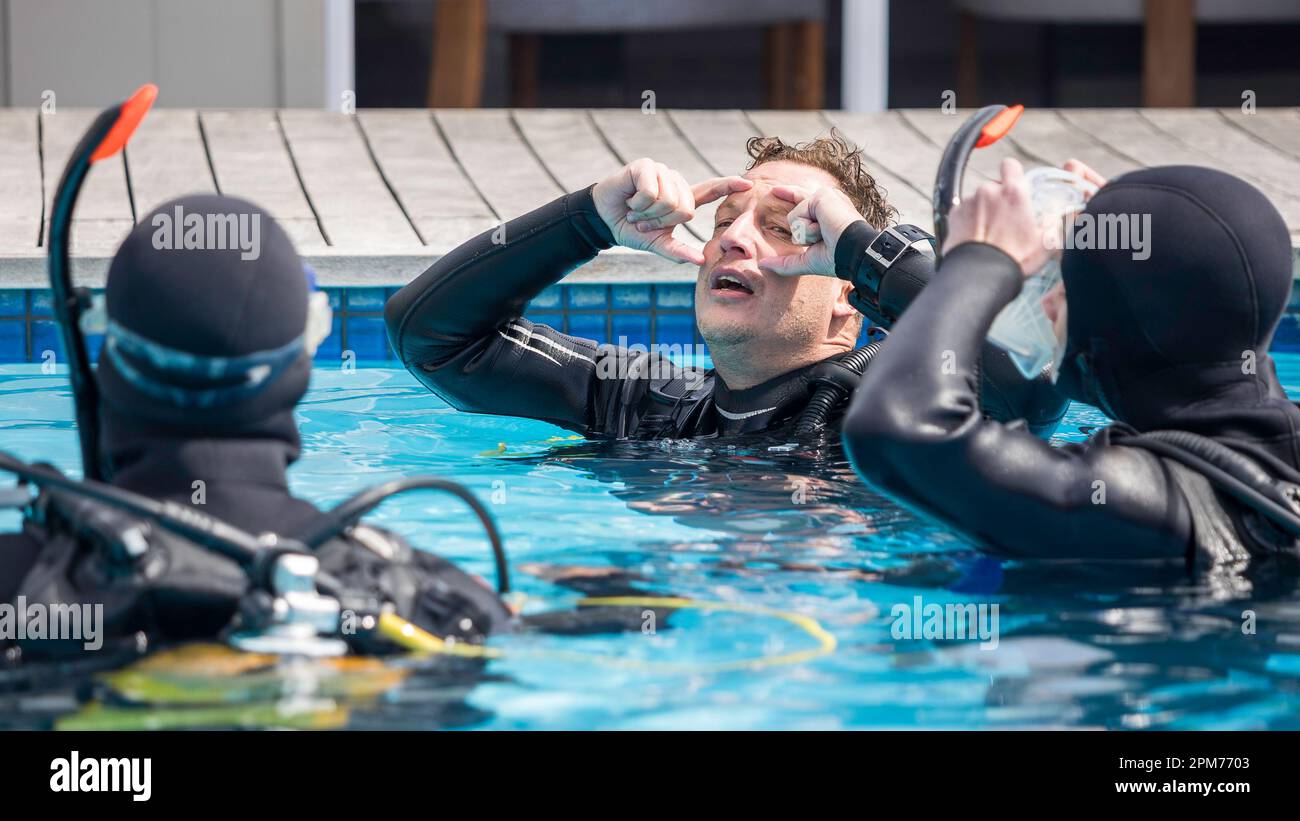 Instructeur de plongée en scaphandre enseignant et expliquant aux élèves votre masque de plongée dans la piscine avec sa tête inclinée vers l'arrière Banque D'Images