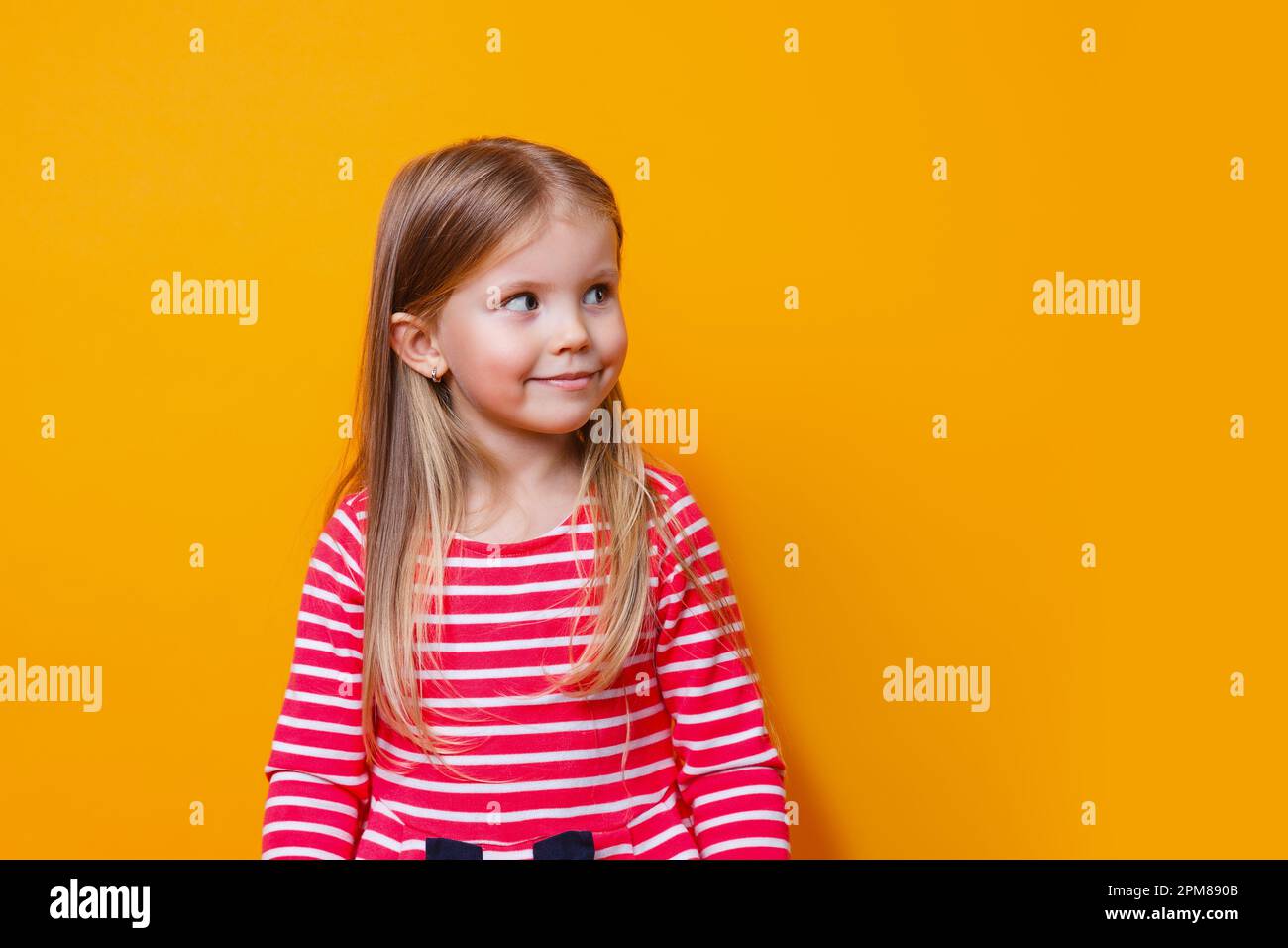 Gros plan portrait de l'enfant adorablel en robe rouge regardant loin avec sourire insouciant heureux sur le studio backgrouind jaune Banque D'Images