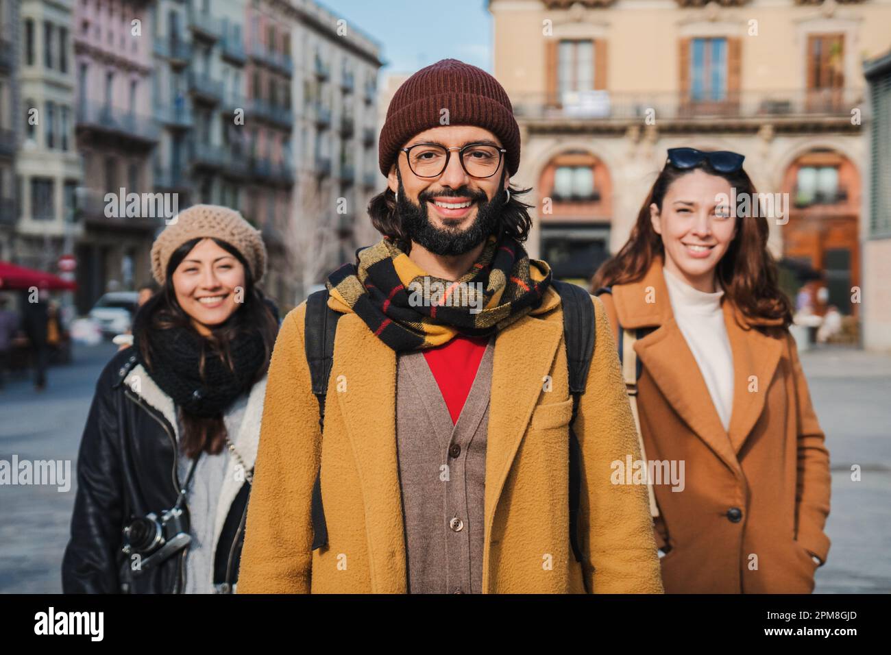 Portrait d'un groupe de jeunes heureux souriant ensemble et regardant l'appareil photo debout à l'extérieur. Vue de face de trois hipsters adorables en voyage dans la ville européenne. Au premier plan, un homme barbu. Photo de haute qualité Banque D'Images