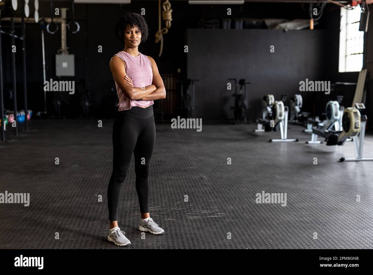 Portrait complet de jeune femme biraciale confiante avec les bras croisés debout dans la salle de gym Banque D'Images
