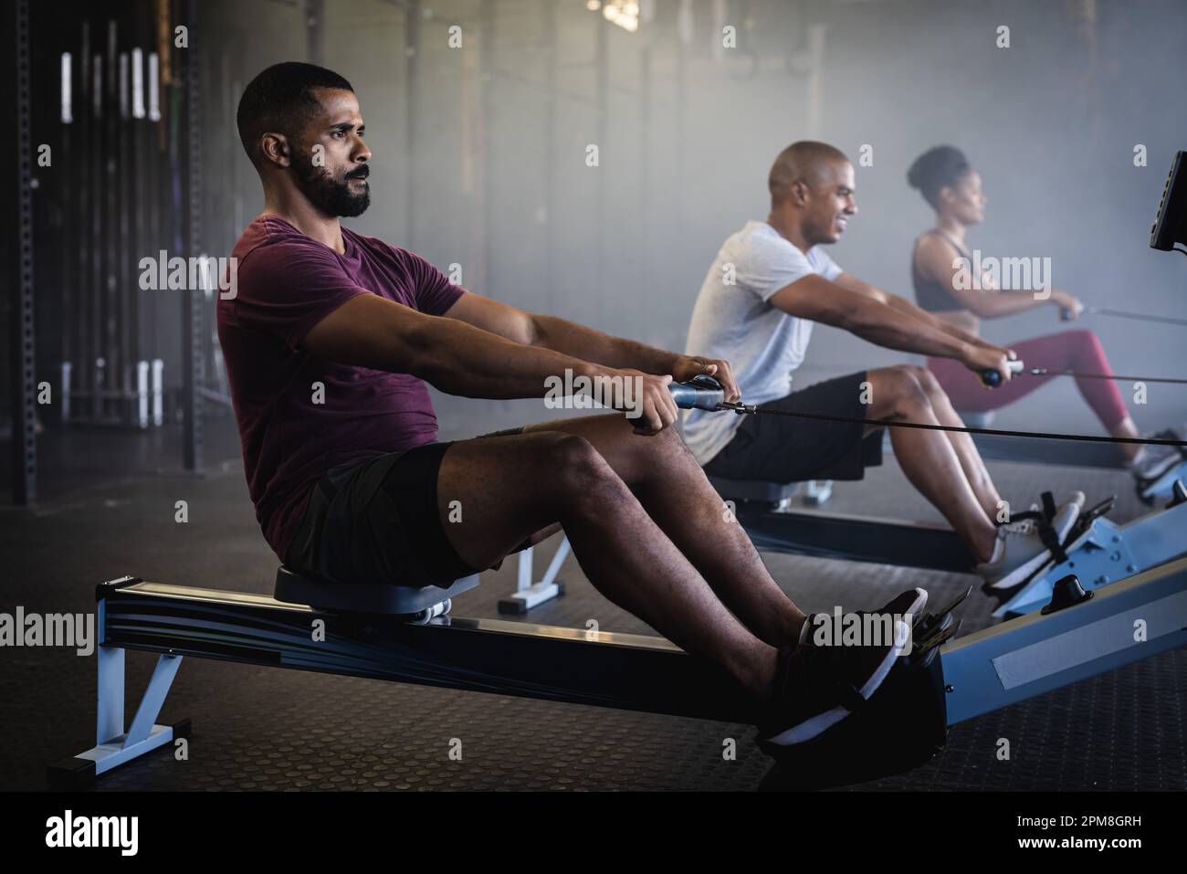 Vue latérale du jeune homme et femme biracial s'exerçant sur des rameurs dans la salle de gym, espace copie Banque D'Images