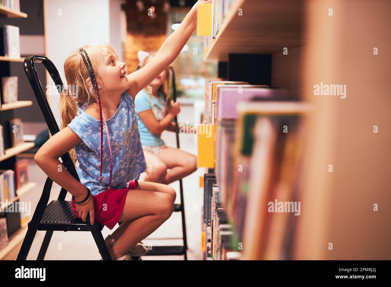Écolières à la recherche de livres dans la bibliothèque de l'école. Étudiants choisissant des livres. L'éducation élémentaire. Faire des devoirs. Apprendre à partir de livres. Retour à l'école Banque D'Images