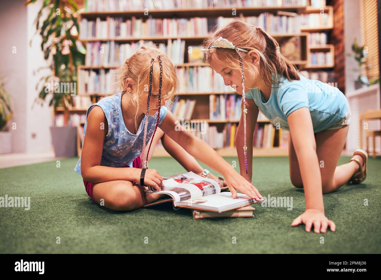 Deux écolières lisent des livres dans la bibliothèque de l'école. Les élèves de l'école primaire apprennent à partir de livres. Élèves faisant leurs devoirs. Les enfants s'amusent avec des livres Banque D'Images