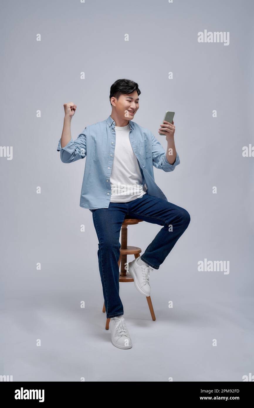 Heureux homme asiatique excité à la recherche à son smartphone et à élever son bras jusqu'à la célébration du succès Banque D'Images