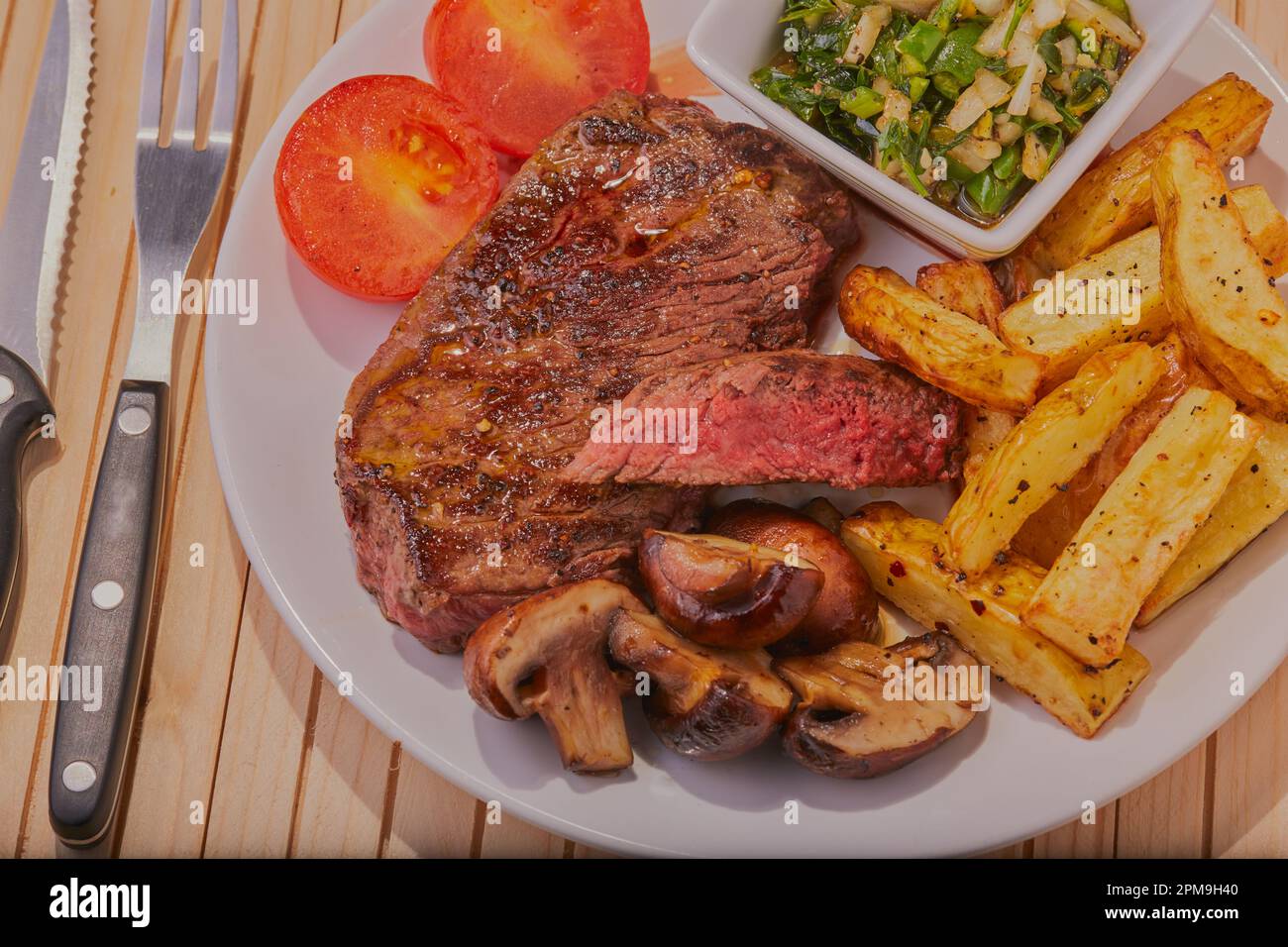 Steak de croupe rare moyen avec frites, champignons et tomates avec une sauce chimichurri. Banque D'Images