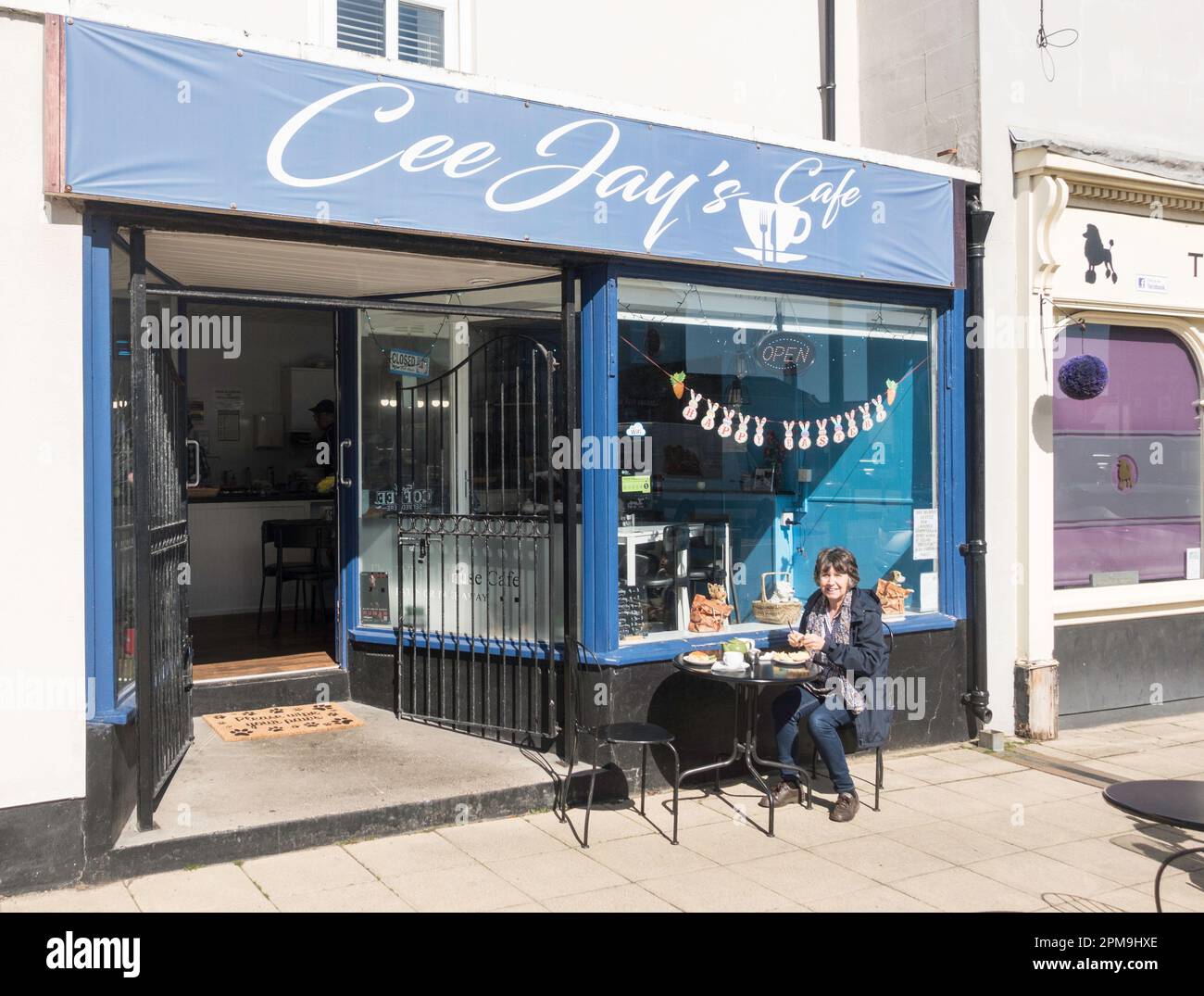 Femme d'âge mûr assise à l'extérieur du café de CEE Jay à Front Street, Newbiggin by the Sea, Northumberland, Angleterre, Royaume-Uni Banque D'Images