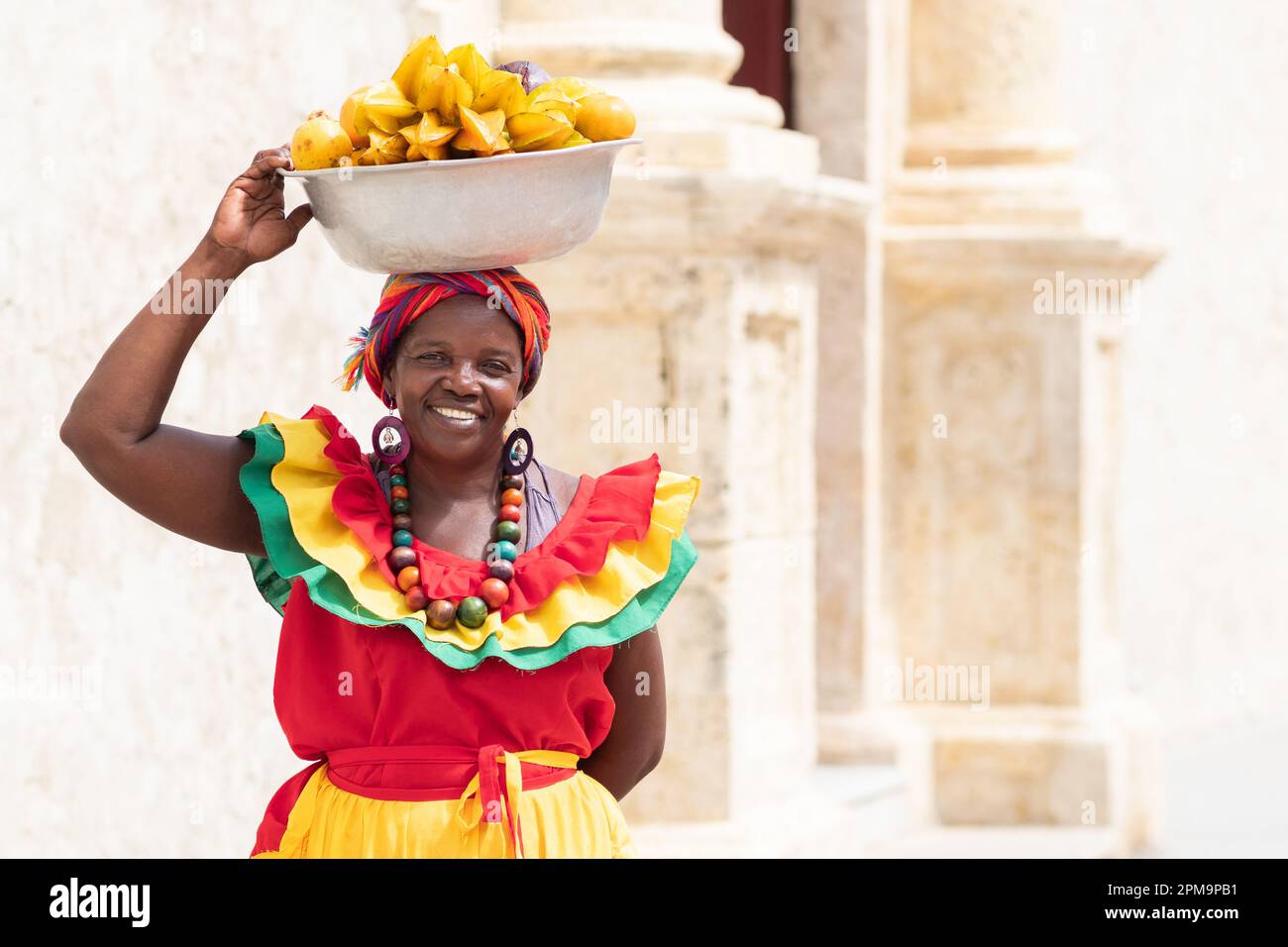 Le vendeur de rue de fruits frais Palenquera souriant se trouve dans la vieille ville de Carthagène, en Colombie. Femme afro-colombienne gaie en costumes traditionnels. Banque D'Images