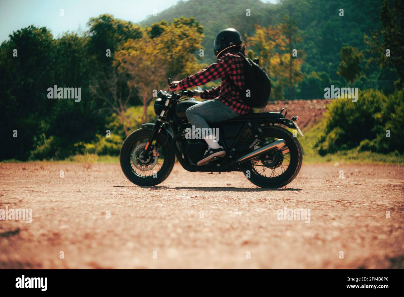 Des hommes qui font de la moto personnalisée sur une route de sable avec un fond de forêt verte Banque D'Images