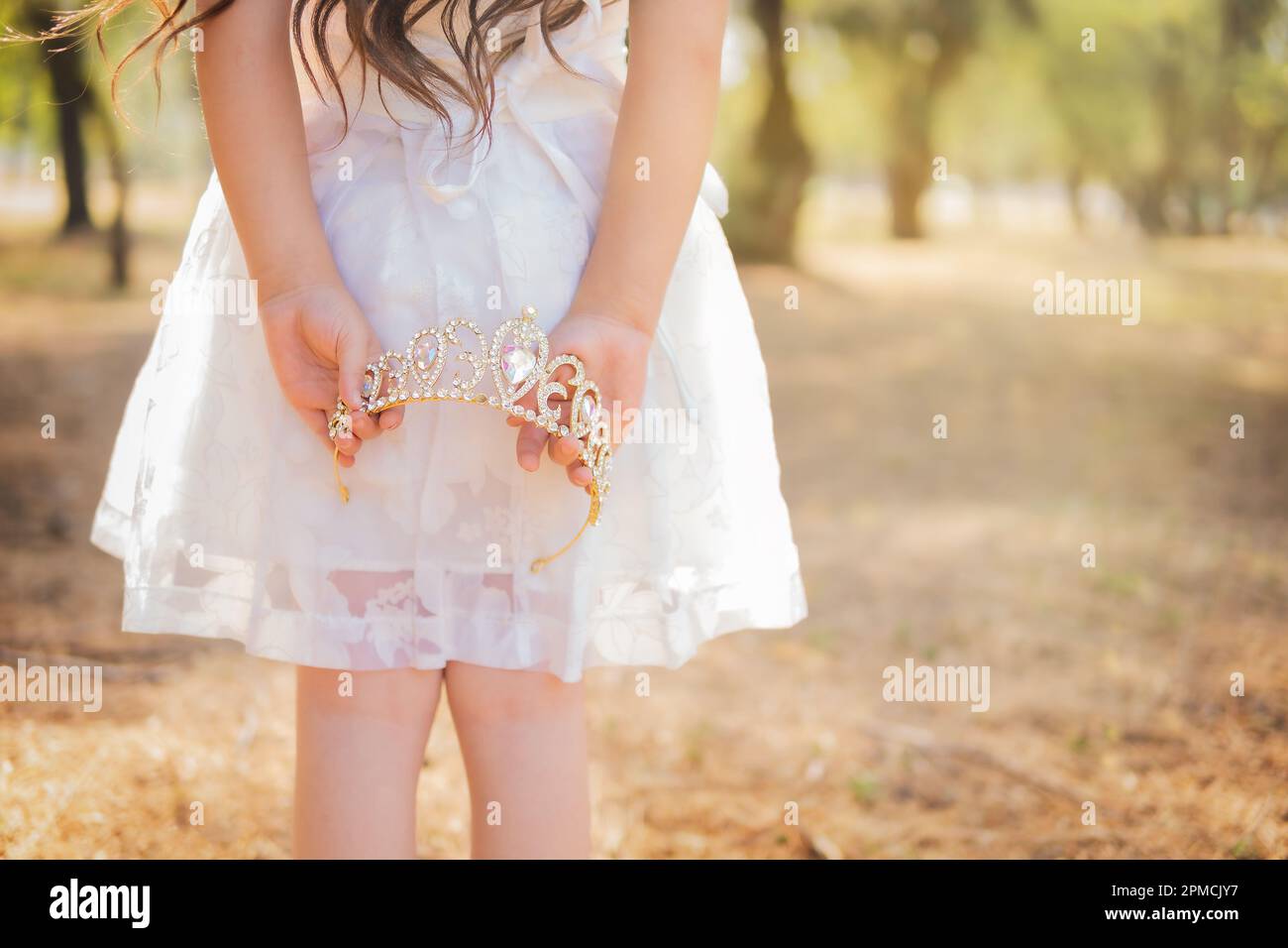 Petite fille en robe blanche est sur son dos tenant une couronne de princesse, dans une forêt rêveuse, espace de copie, thème de jour d'enfants. Banque D'Images