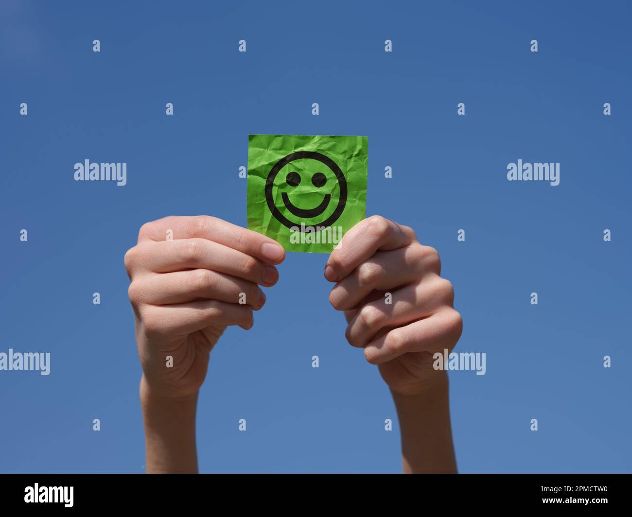 Un garçon tenant une note en papier vert avec un visage heureux dans ses mains contre le ciel bleu. Gros plan. Banque D'Images