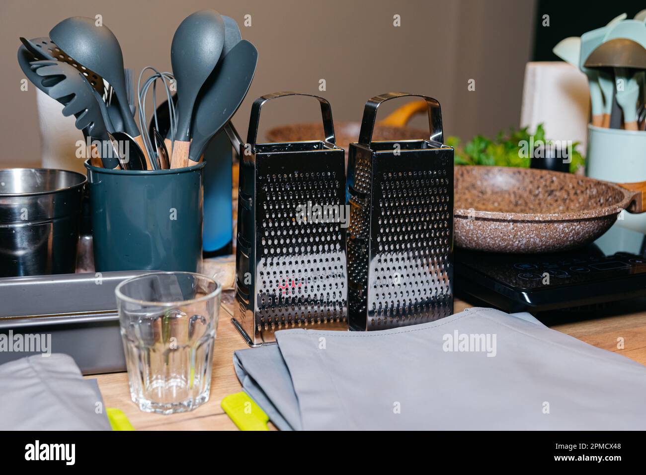 Les ustensiles de cuisine et les outils comme les spatules ou le fouet, le tablier gris et deux râpes en acier à main sont assis sur une table avant le cours de cuisine. Maître culinaire cla Banque D'Images