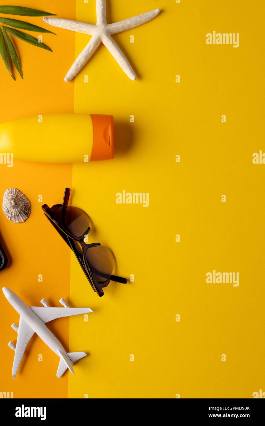 Modèle d'avion, lunettes de soleil, écran solaire, plante et coquillages sur fond jaune avec espace de copie Banque D'Images