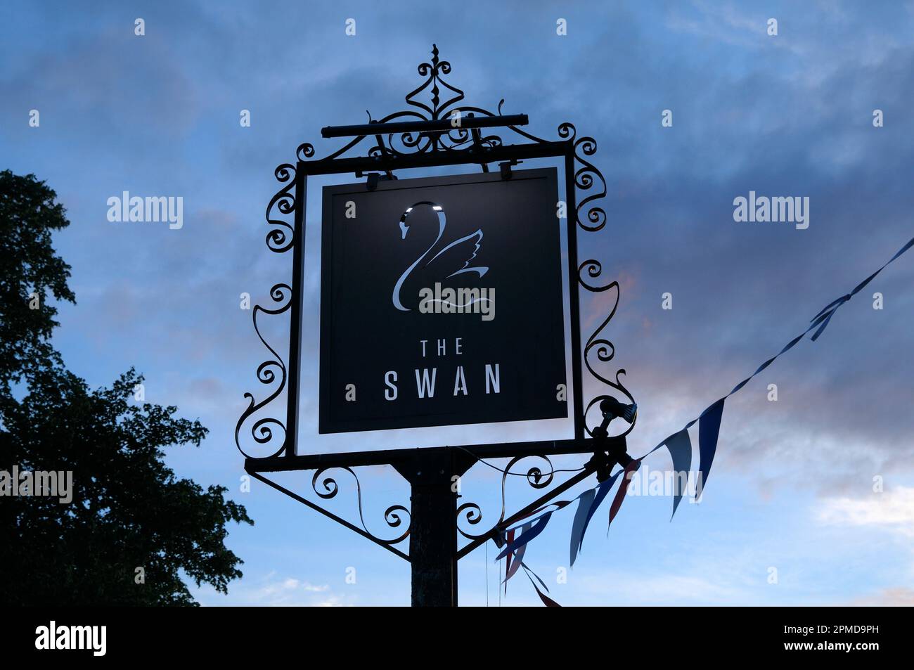 Un panneau métallique orné au crépuscule devant le Swan, un pub et restaurant moderne dans le village de Cotswold de Broadway, Cotswolds, Worcestershire, Angleterre, Royaume-Uni Banque D'Images