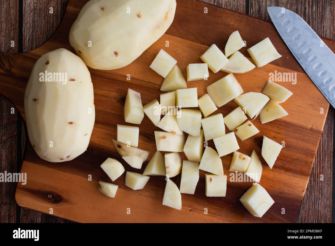 Pommes de terre Russet pelées et coupées en cubes sur une planche à découper en bois : pommes de terre fraîches hachées en petits cubes avec un couteau de cuisine et une planche à découper Banque D'Images