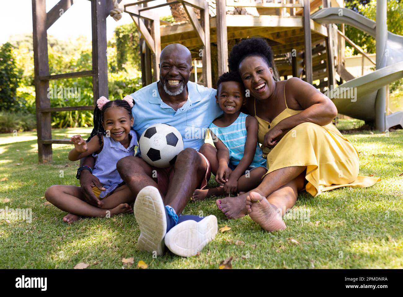 Joyeux grands-parents et petits-enfants afro-américains avec un ballon assis sur des terres herbeuses dans le parc Banque D'Images