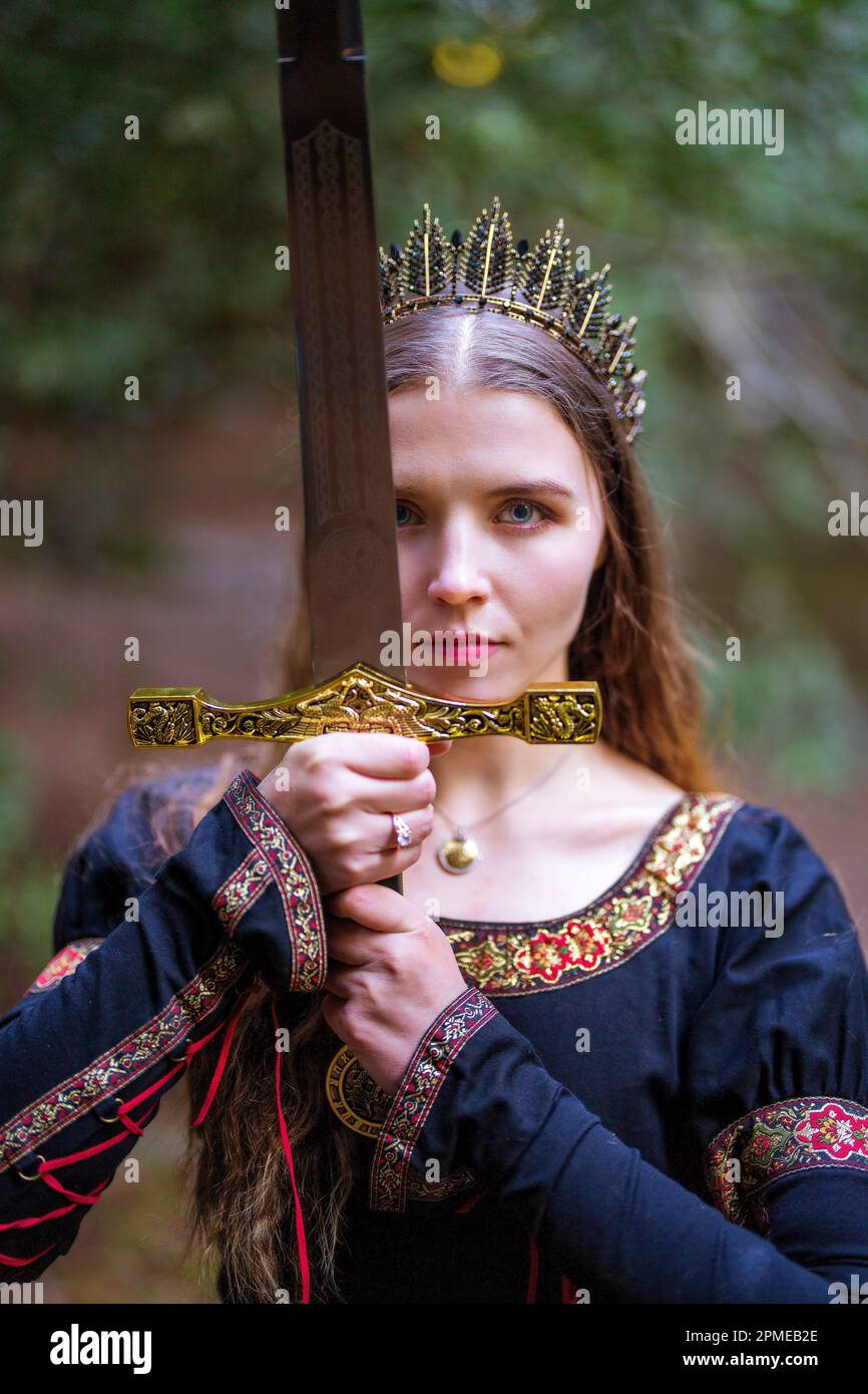 Jeune femme en costume Queen de conte de fées avec Crown brandissant un grand Broadsabre | tons chauds Banque D'Images