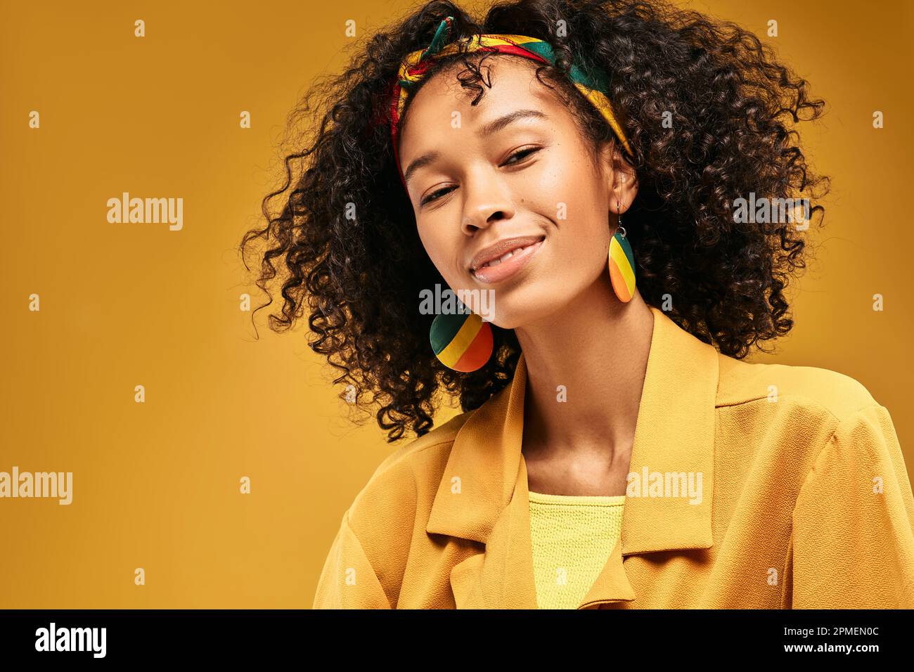 Portrait d'une fille rastafarienne avec une coiffure bouclés, de beaux yeux et de belles lèvres en regardant l'appareil photo sur fond jaune. Un sourire magnifique face à la mignonne Banque D'Images
