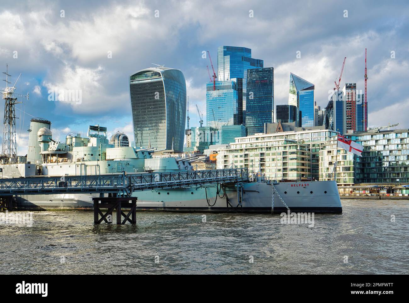 Les canons du navire de guerre HMS Belfast de la Seconde Guerre mondiale offrent un contraste saisissant avec l'élégante toile de fond architecturale du quartier financier de Londres. Banque D'Images