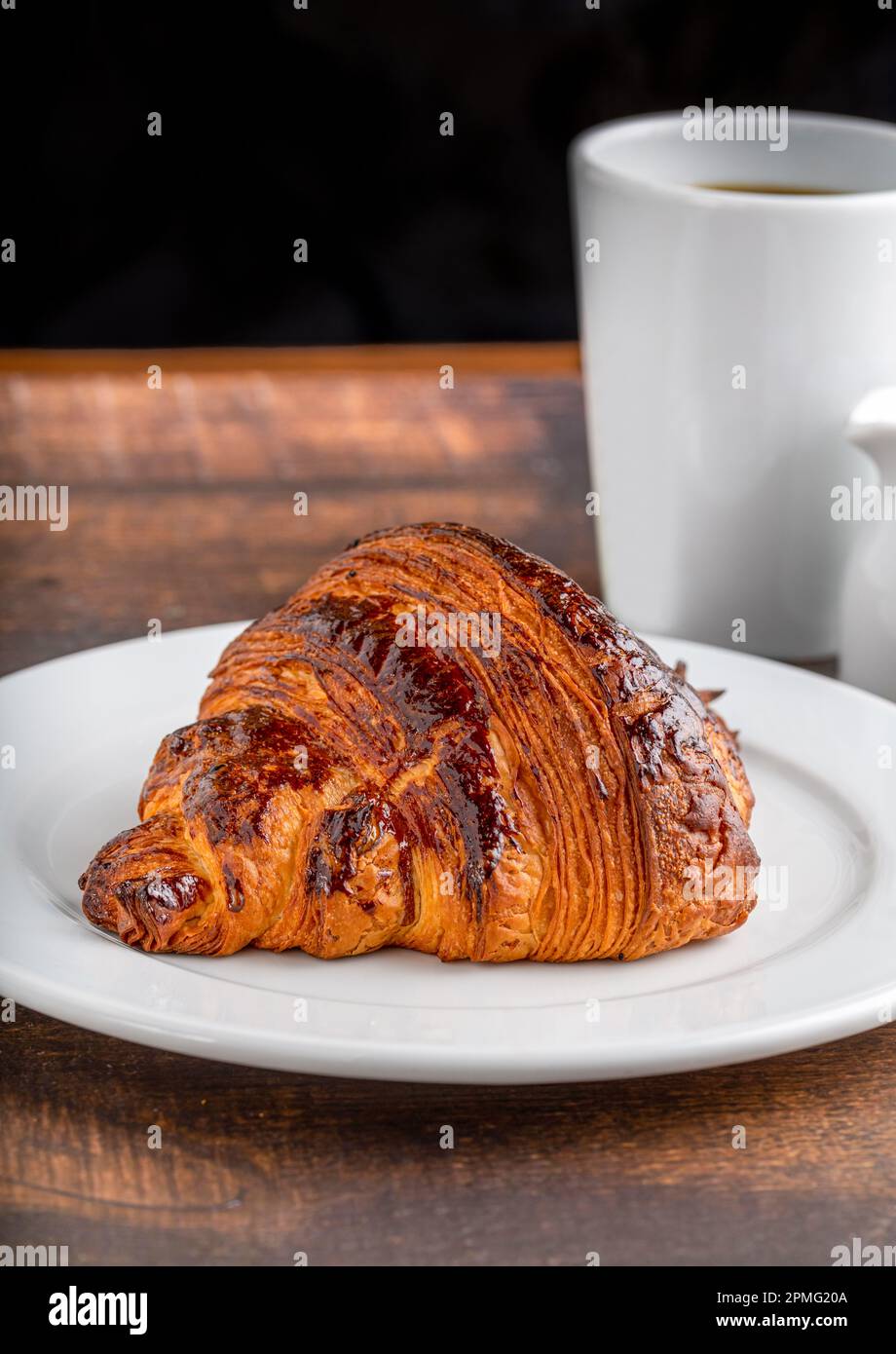 Croissant avec café à côté sur une table en bois Banque D'Images