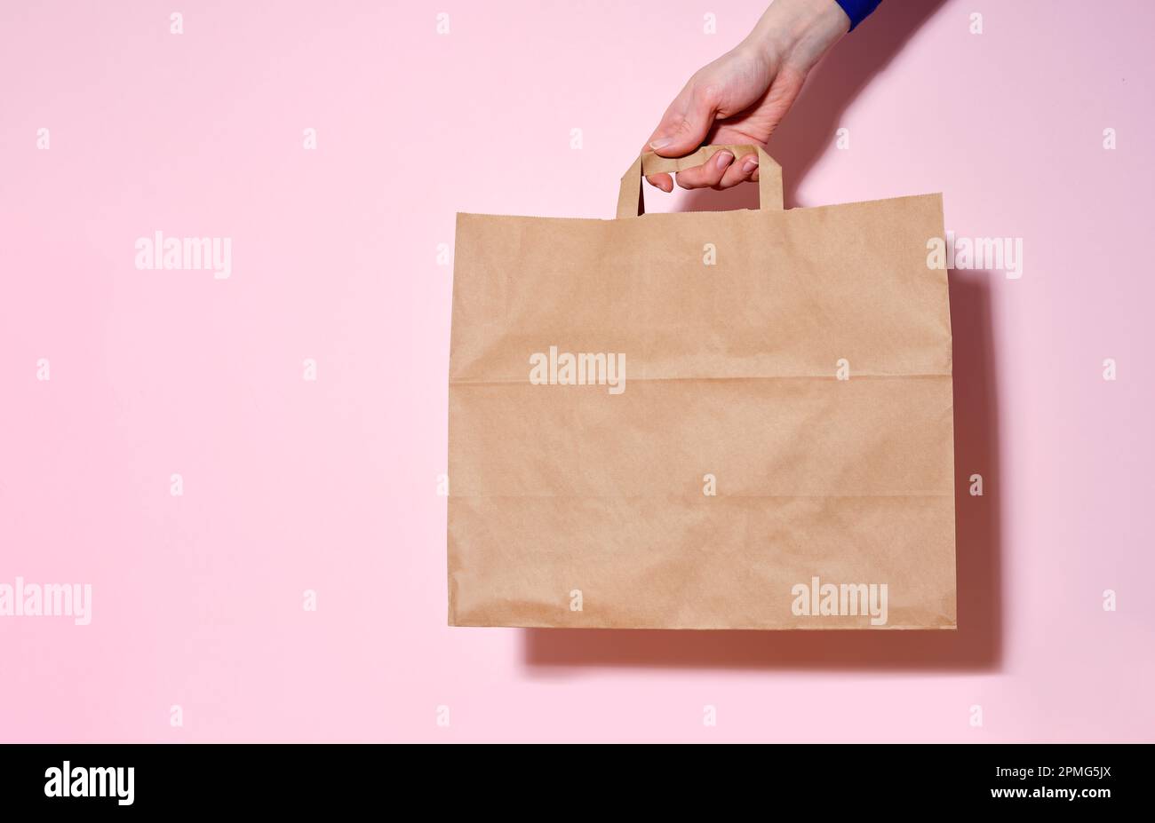 Main femelle tenant un sac en papier avec les articles livrés. Arrière-plan rose, espace de copie Banque D'Images