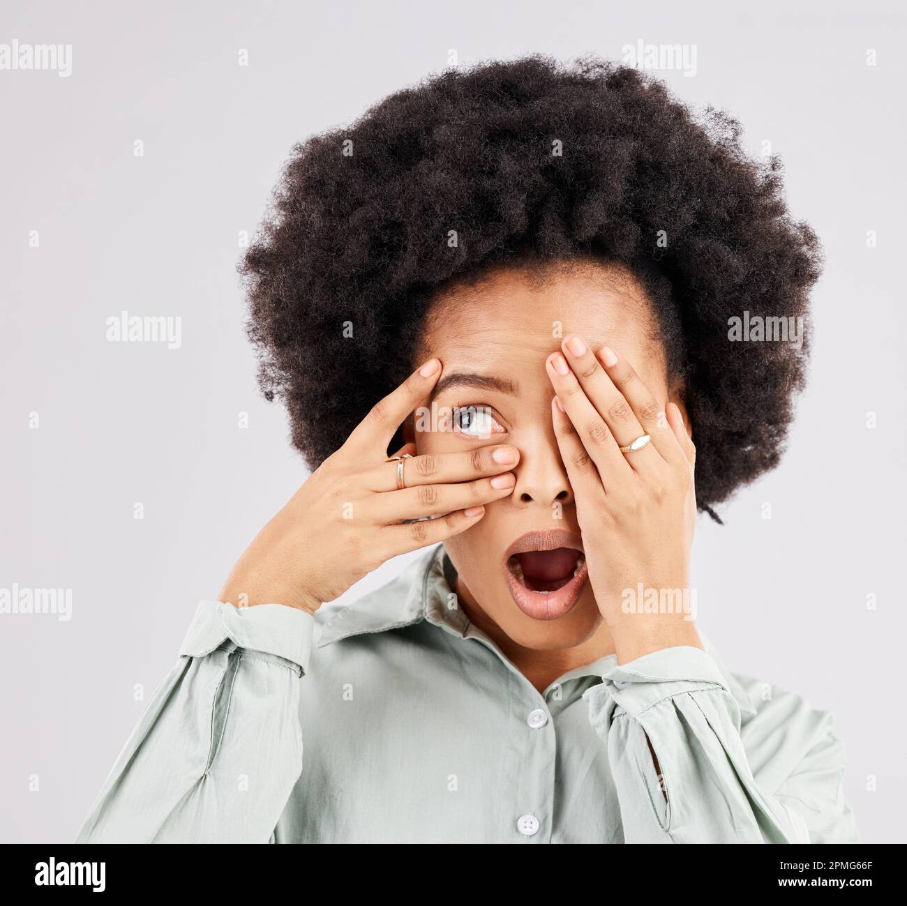 Choc, peur et une femme noire regardant à travers les mains isolées sur un fond blanc dans un studio. Wow, effrayant et une fille africaine couvrant les yeux avec un Banque D'Images