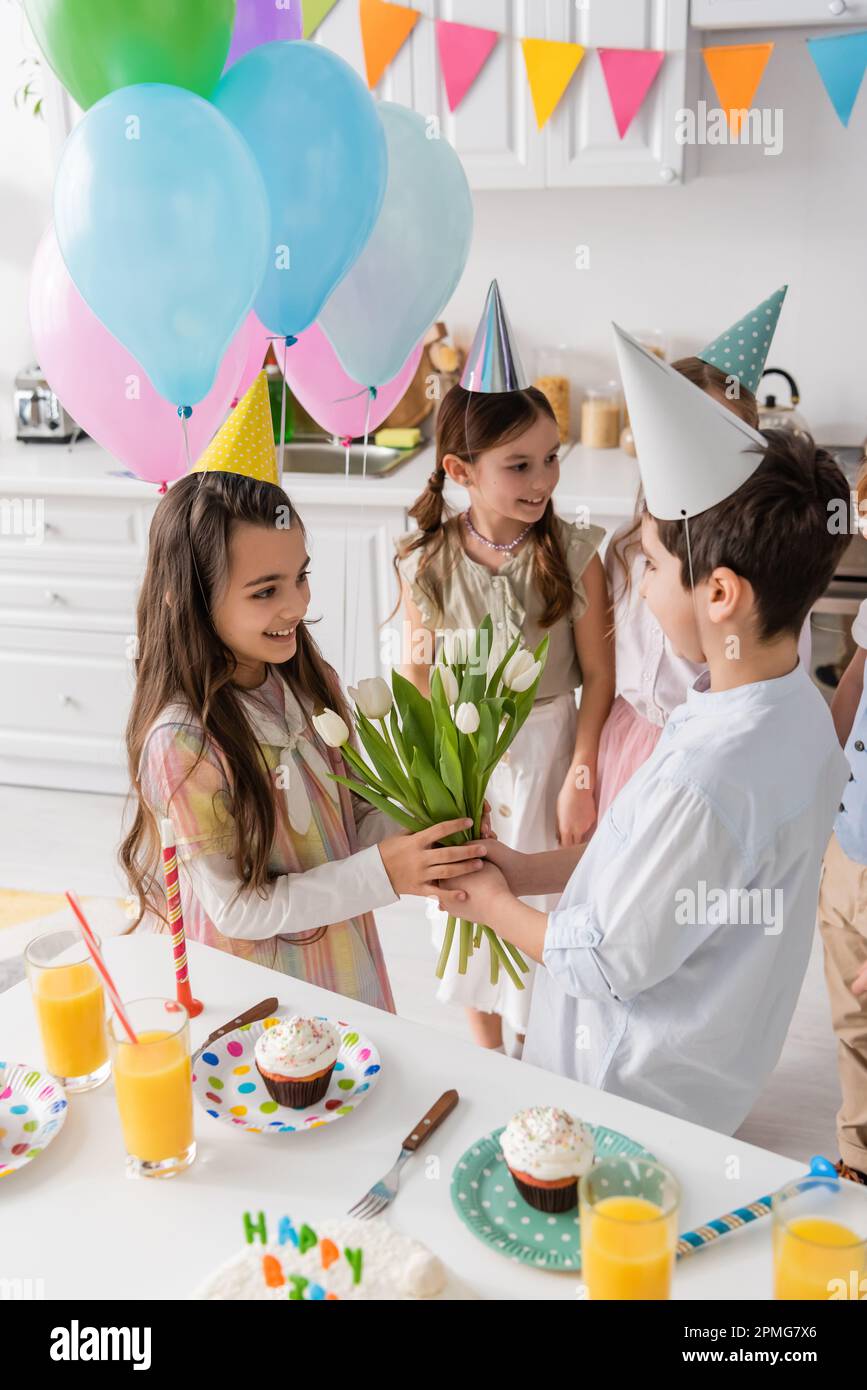 préteen garçon donnant des tulipes à joyeux anniversaire fille près des enfants sur fond flou, image de stock Banque D'Images