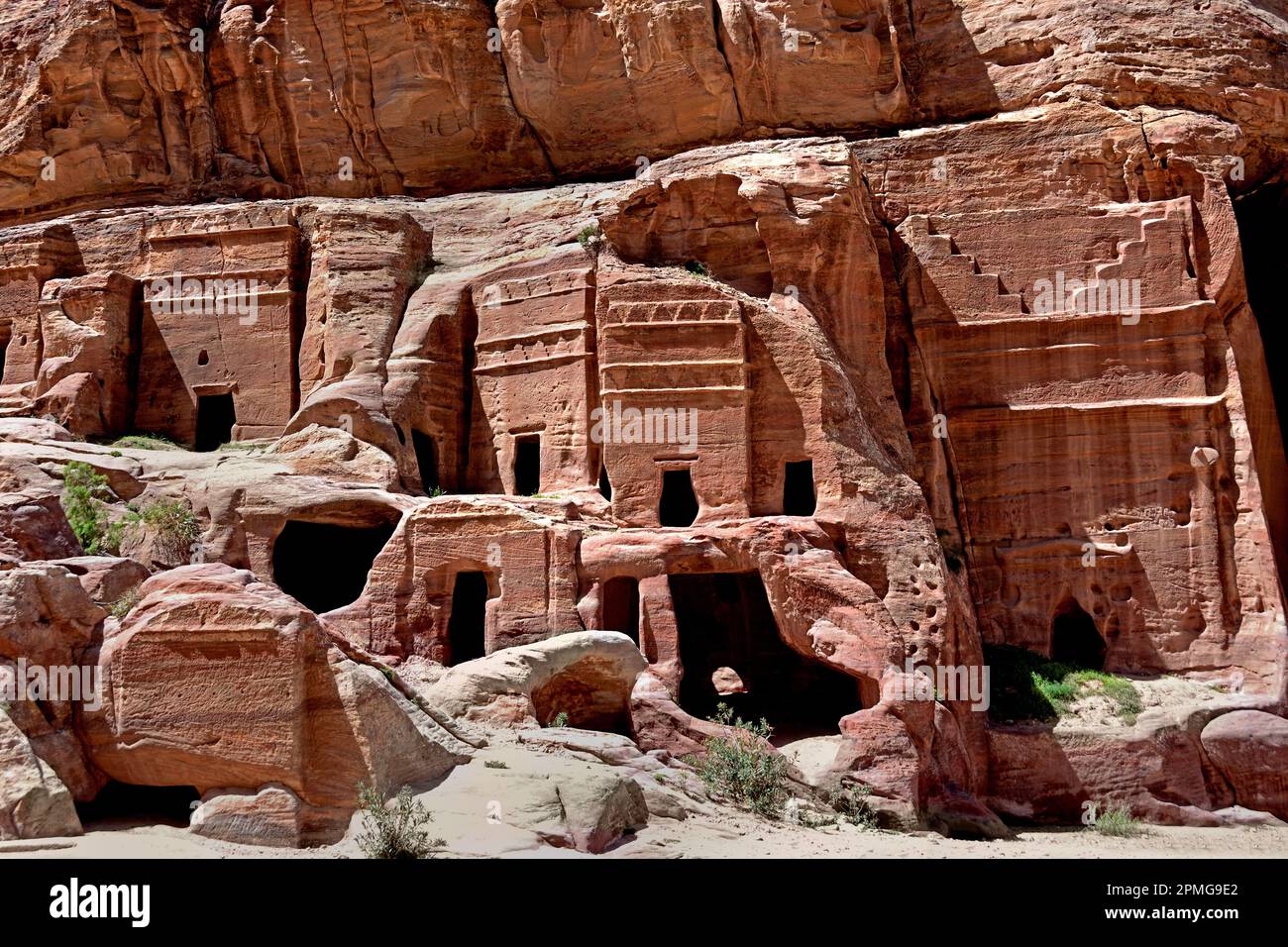 Rue des Façades présentant des rangées de petites tombes nabatéennes taillées dans la roche, creusées dans les immenses falaises de grès sous un ciel bleu clair à Petra, en Jordanie. Banque D'Images