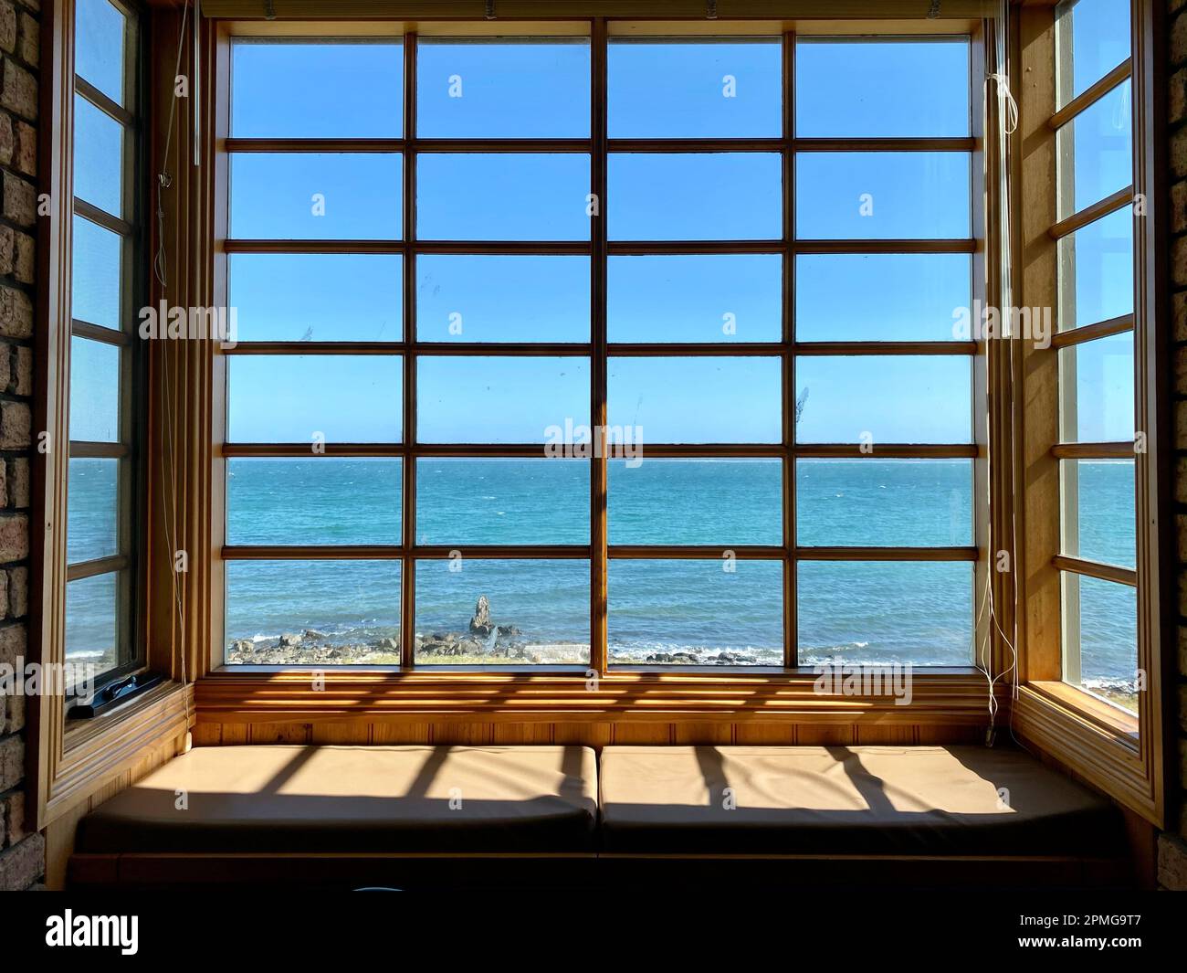 Une grande fenêtre ouverte dans un bâtiment en briques offre une vue imprenable sur l'océan en contrebas Banque D'Images