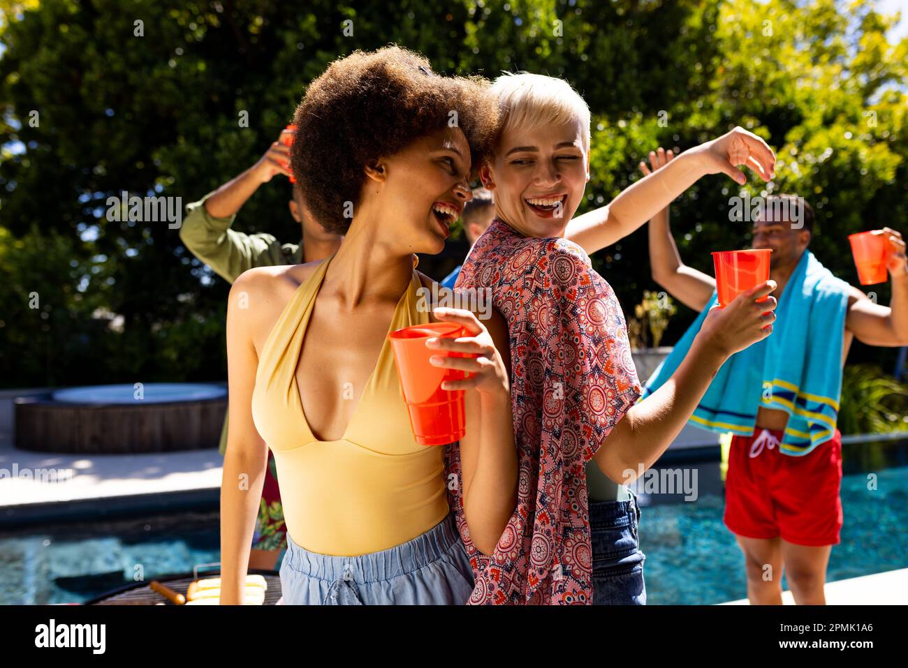 Joyeux groupe d'amis divers ayant la fête au bord de la piscine, dansant dans le jardin Banque D'Images