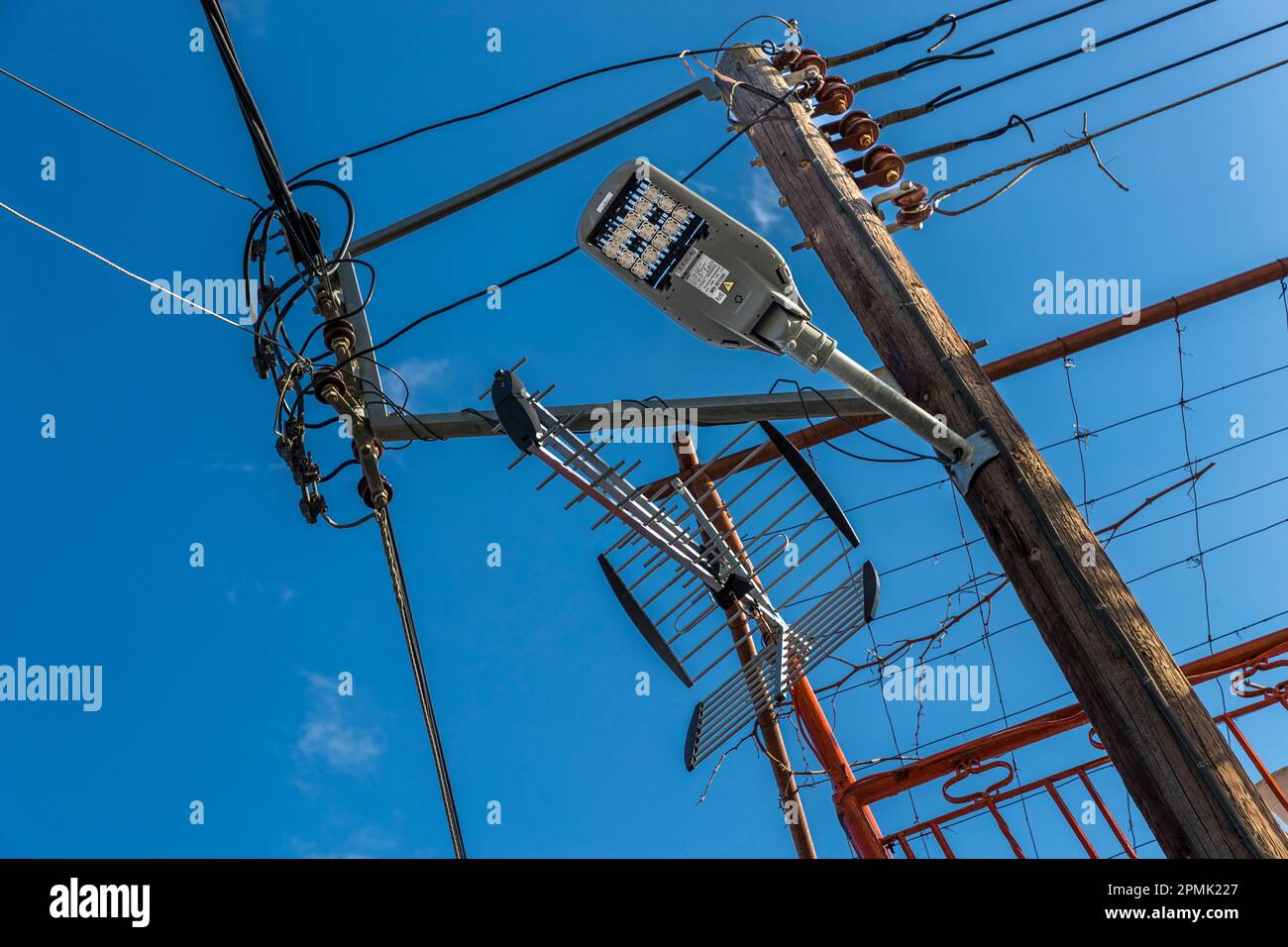 Un enchevêtrement de câbles, d'antennes et de lampes – mais au moins avec des lumières LED – pend d'un poteau en bois à Omodos, République de Chypre. Banque D'Images