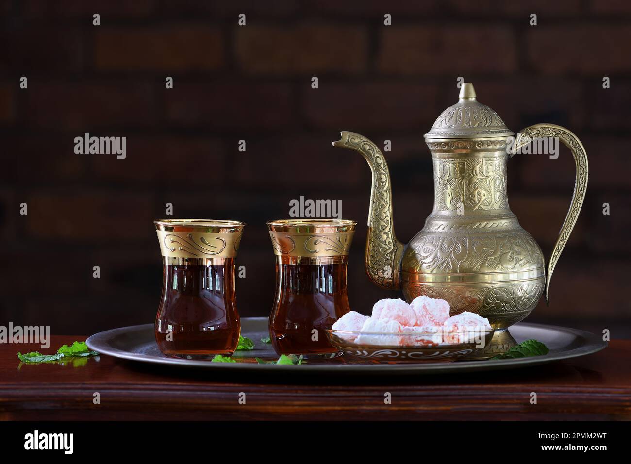 Théière turque ornée, classique et festive, deux verres et délices turcs traditionnels sur un plateau et une table en bois, dans un éclairage tamisé Banque D'Images