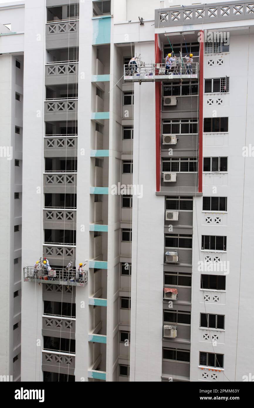 Vue verticale de l'ascenseur d'échafaudage avec des peintres peignant une nouvelle couche de peinture sur l'extérieur du boîtier pour donner un look frais. Singapour. Banque D'Images