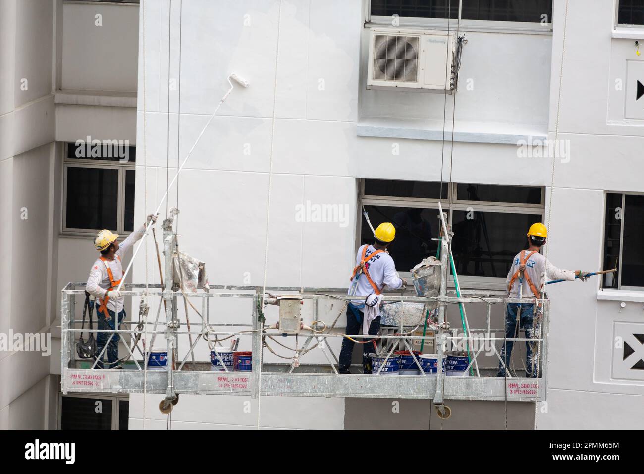 Gros plan de l'ascenseur d'échafaudage avec trois peintres peignent une nouvelle couche de peinture sur l'extérieur du boîtier pour donner un look propre. Singapour. Banque D'Images