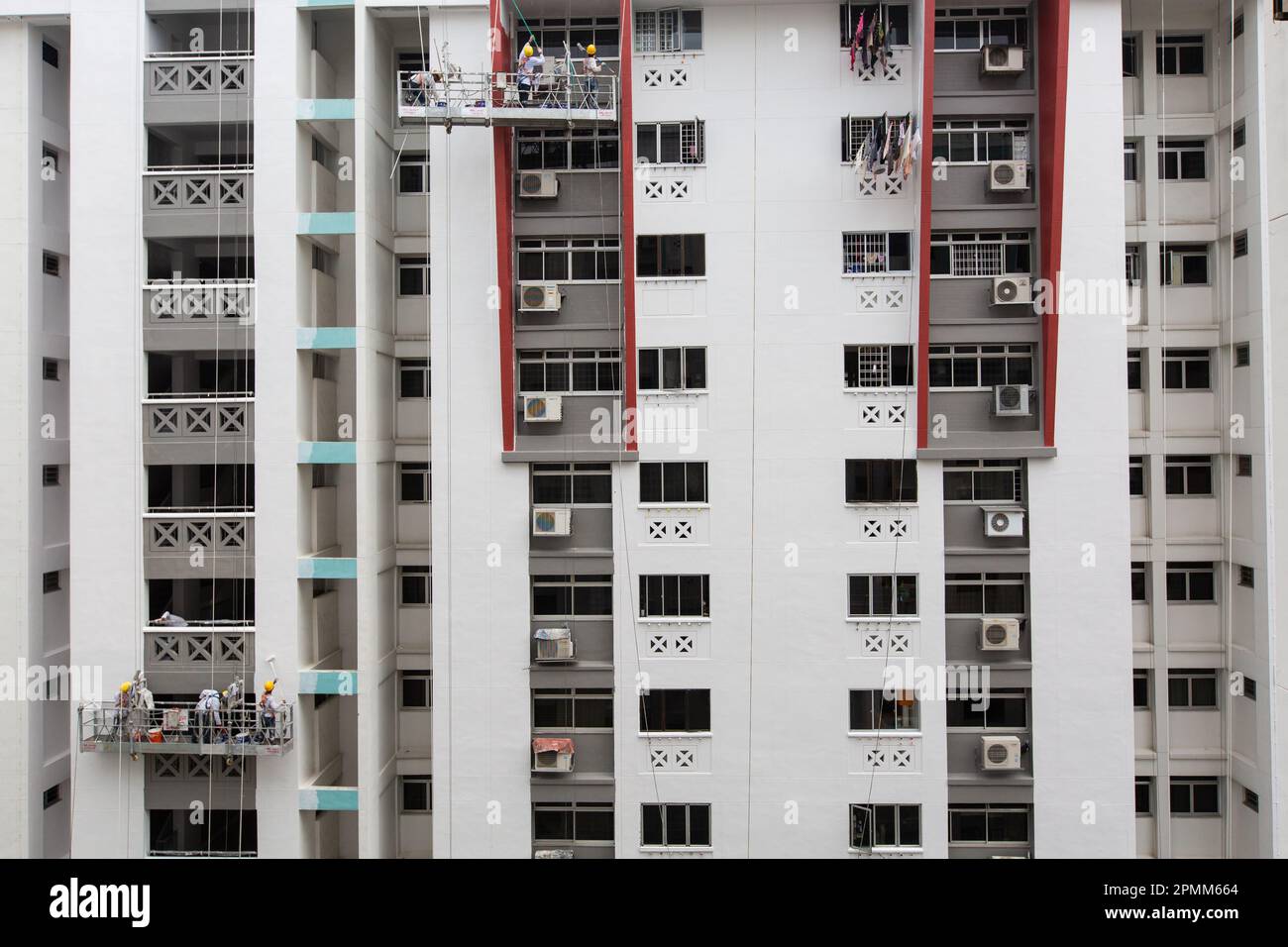 Vue large de 2 ascenseurs d'échafaudage suspendus à l'extérieur d'un bloc, les ouvriers sont occupés à peindre le bâtiment avec une couche de peinture fraîche, Singapour. Banque D'Images