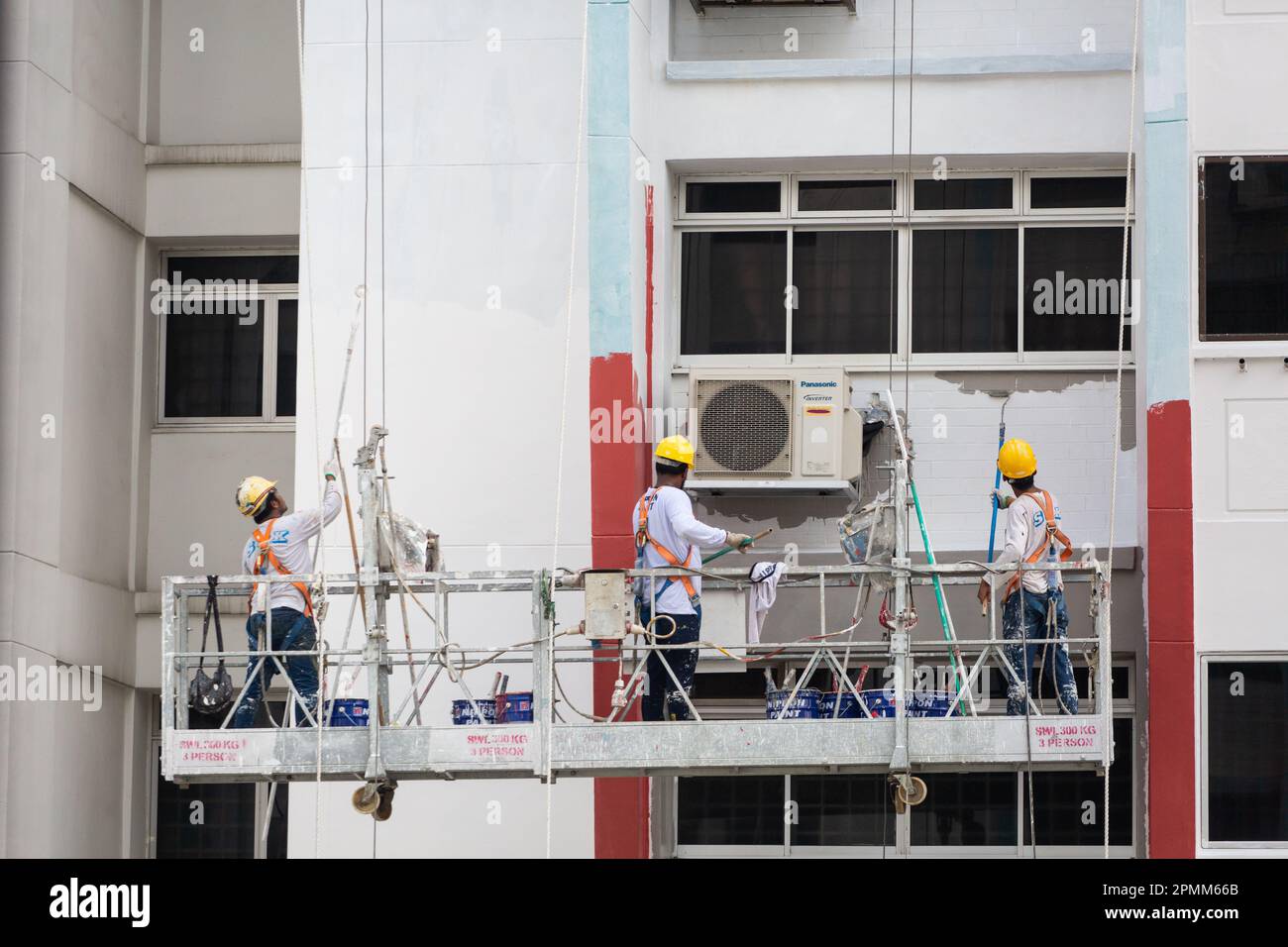 Gros plan de l'ascenseur d'échafaudage avec 3 peintres peignent une nouvelle couche de peinture sur l'extérieur du boîtier pour donner un nouveau look. Singapour. Banque D'Images
