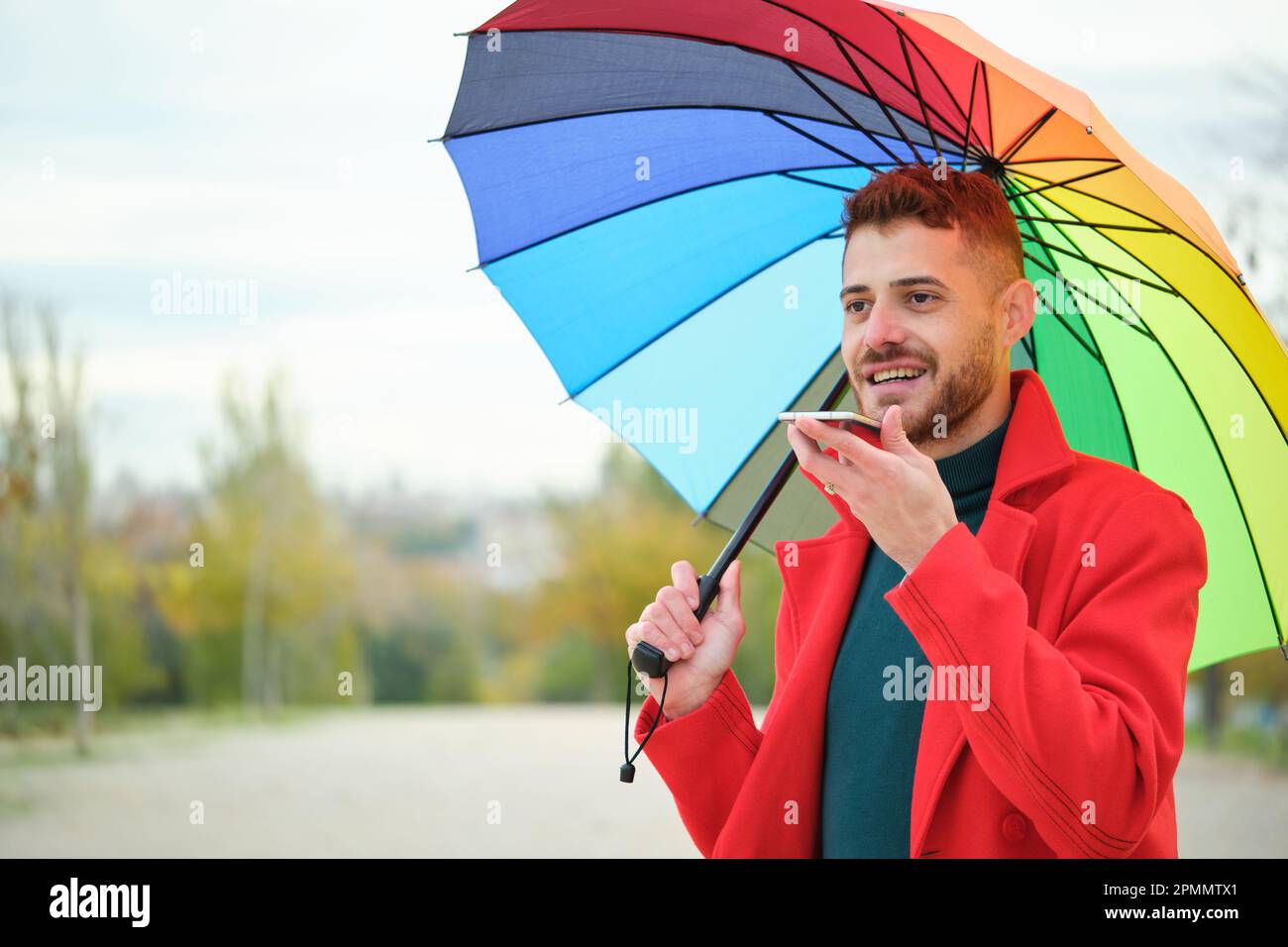 Jeune latino-américain avec un manteau rouge et un parapluie arc-en-ciel  enregistrant un message audio Photo Stock - Alamy