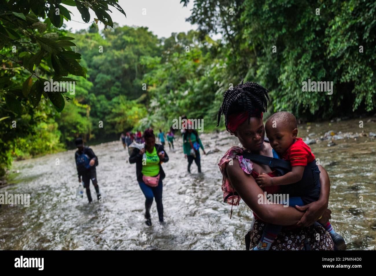 Un migrant haïtien, portant son bébé, marche à travers la rivière dans la jungle sauvage et dangereuse du fossé Darién entre la Colombie et Panamá. Banque D'Images