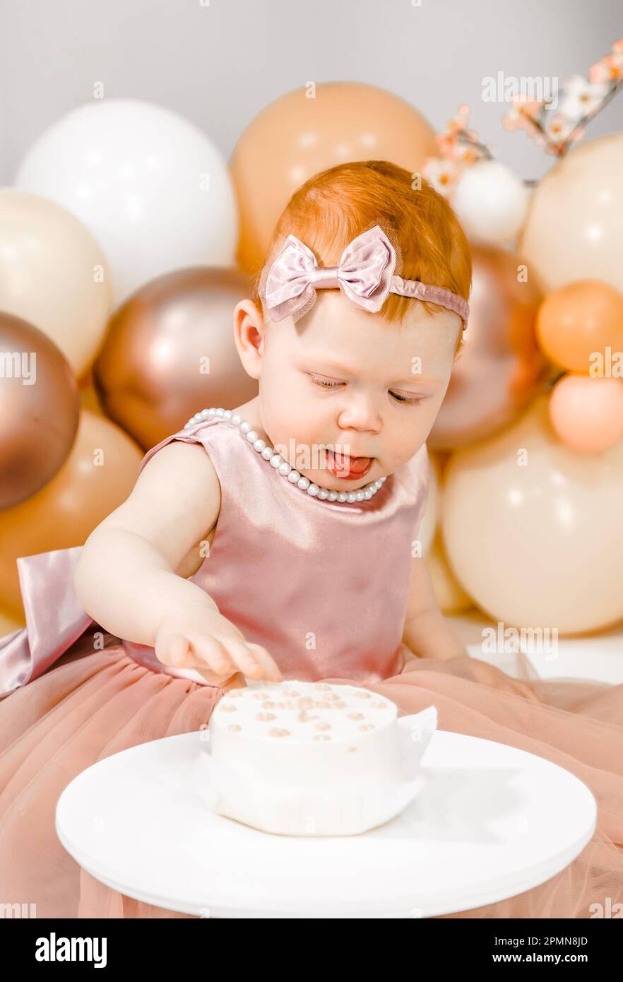 Petite fille à tête rouge fête son premier anniversaire. Cake crash smash, les mains manger. fête de balons familiaux de 1 ans. Séance photo professionnelle. Studio photo Banque D'Images