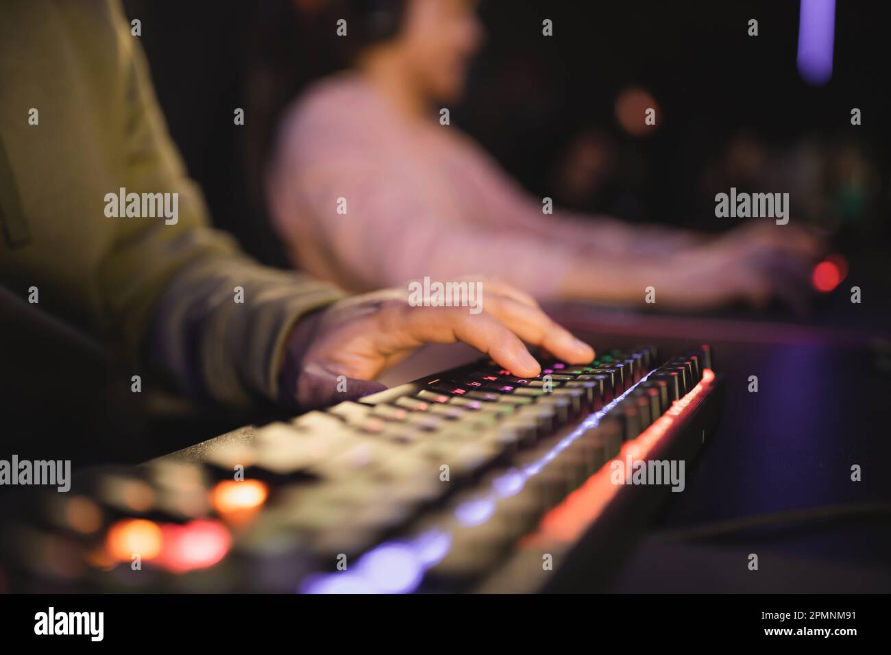 Vue rognée de l'homme en utilisant un clavier d'ordinateur avec éclairage dans cyber club, image de stock Banque D'Images