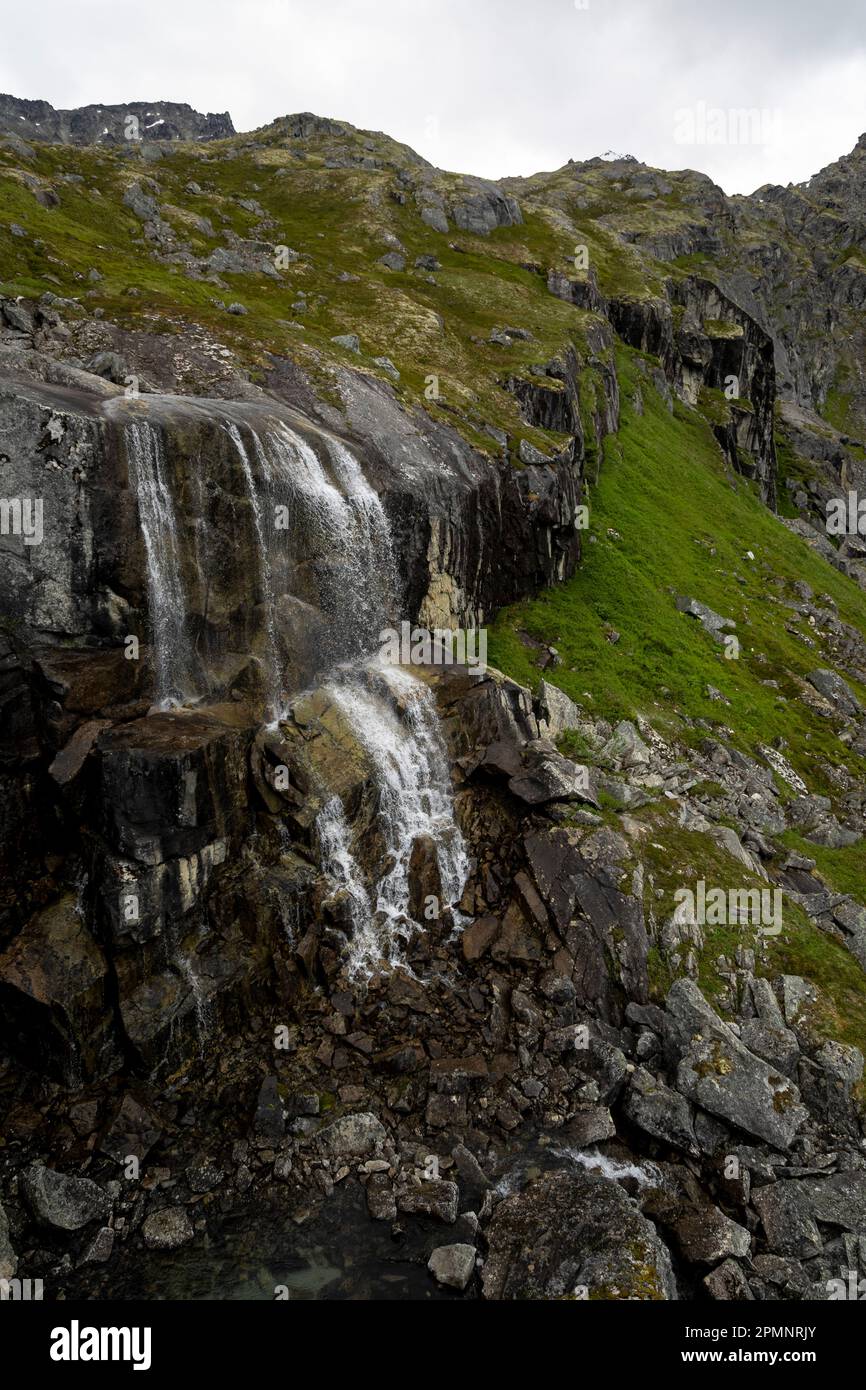 Reed Falls, une chute d'eau glaciaire coulant sur l'herbe couverte, rocheuse à flanc de montagne à Archange Hatcher Pass sous un ciel gris et nuageux près d'Independent... Banque D'Images