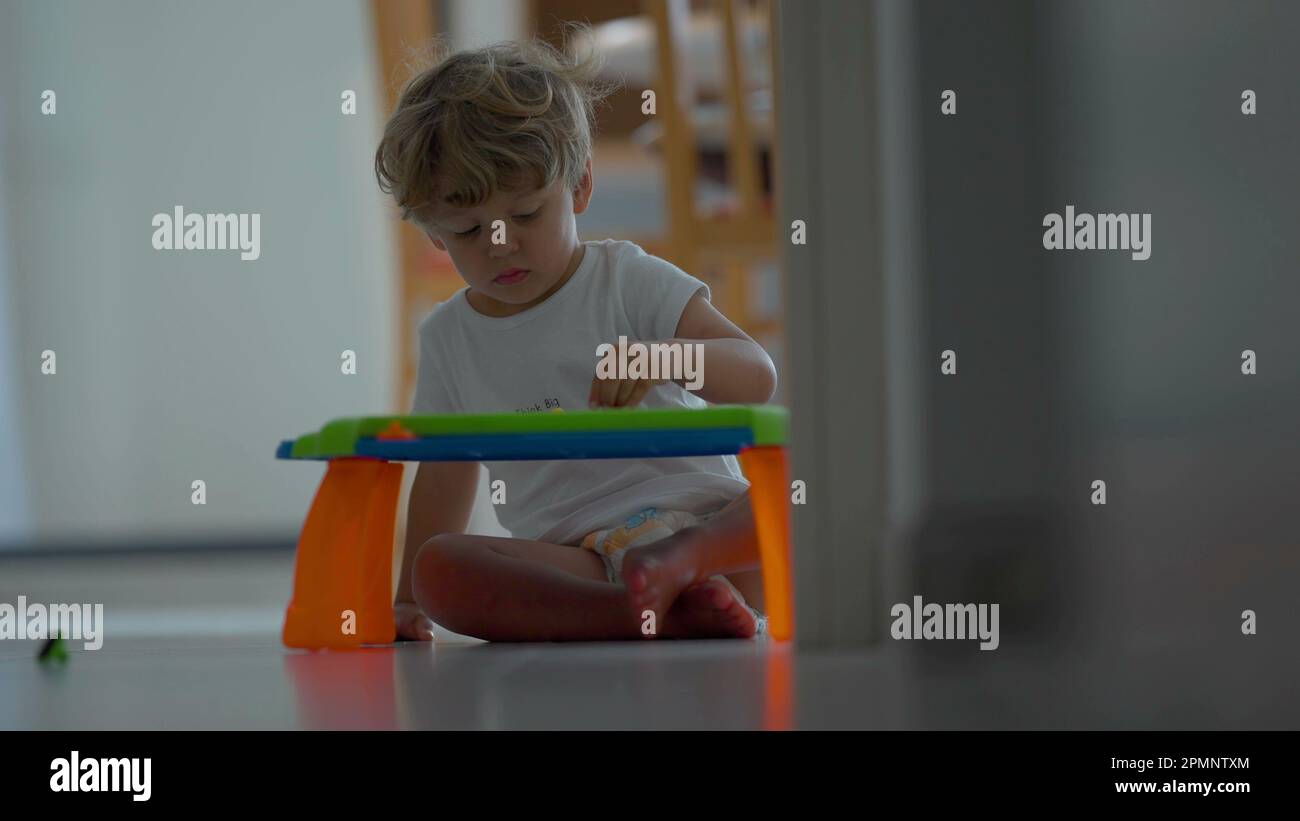 Un enfant assis au sol joue avec un plan magnétique effaçable à la maison. scène de style de vie enfant Banque D'Images