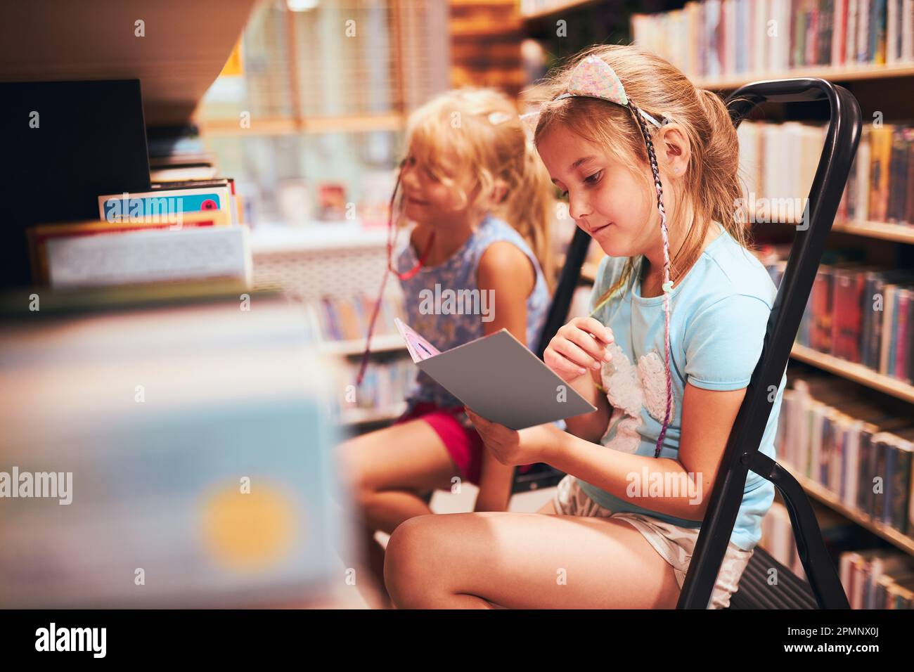 Écolières à la recherche de livres dans la bibliothèque de l'école. Étudiants choisissant des livres de jeu. L'éducation élémentaire. Faire des devoirs. Apprendre à partir de livres. Retour à la goélette Banque D'Images